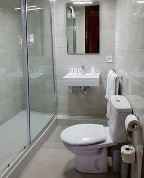 Et badeværelse med toilet, håndvask, brusekabine i glas og et spejl.