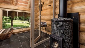 Interior de una cabaña de madera con chimenea, una puerta de vidrio que da al exterior y una cesta de mimbre en el suelo.