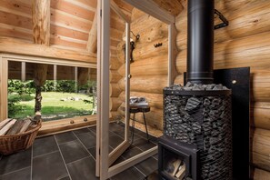L’intérieur d’un chalet en bois, avec une cheminée, une porte vitrée donnant sur l’extérieur et un panier en osier posé sur le sol.