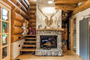 A log cabin interior with a stone fireplace, wooden stairs, and a deer head mounted on the wall.