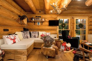 A log cabin interior with a sofa, a television, a fireplace, and a window with a wreath.