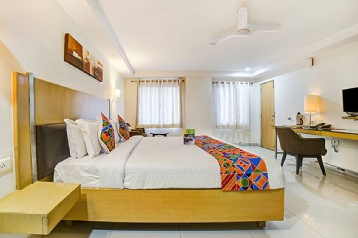 A hotel room with a bed, bedside table, desk, chair, and a TV.