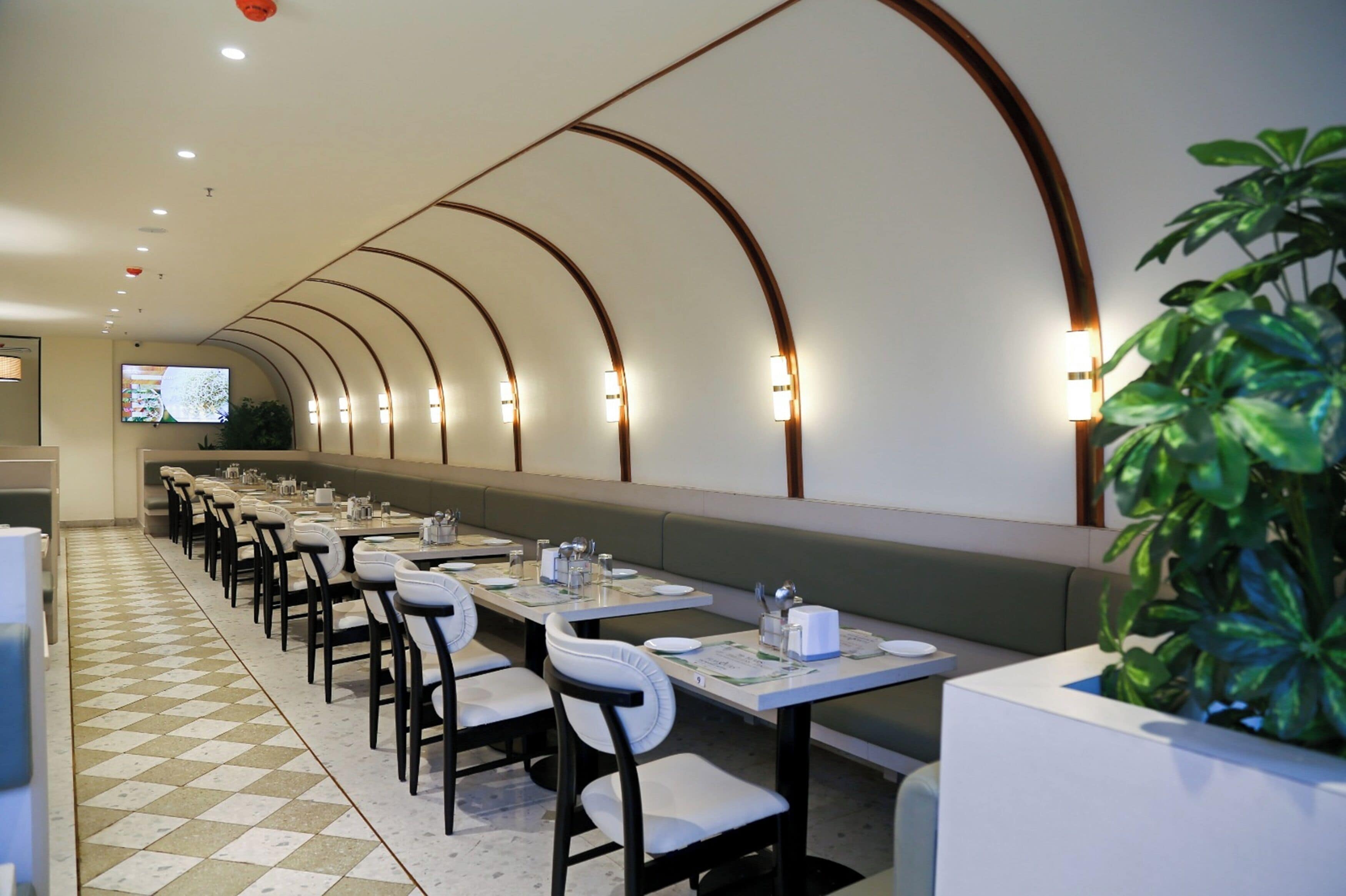 Une grande salle à manger avec des tables et des chaises, un écran de télévision et une plante.