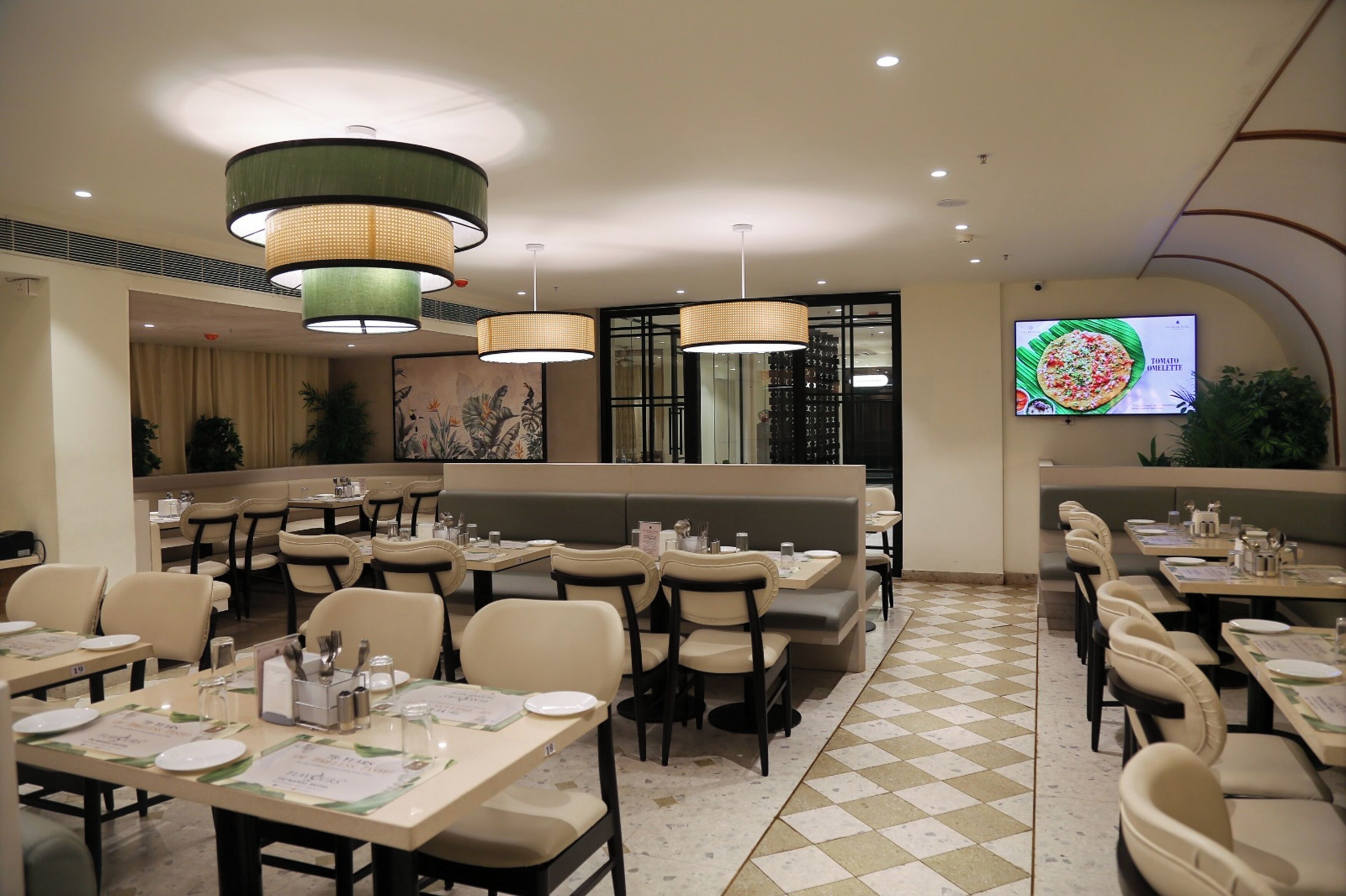 A restaurant with multiple dining tables, chairs, and a large screen displaying a pizza advertisement.