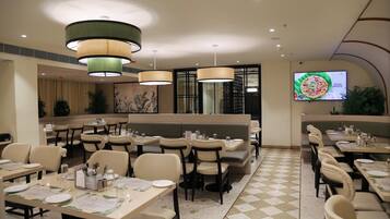 A restaurant with multiple dining tables, chairs, and a large screen displaying a pizza advertisement.