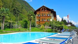 A pool with lounge chairs, a building with balconies, and a mountainous backdrop. - Tannhof (Caldaro Sulla Strada del Vino)