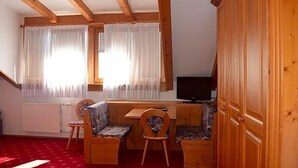 A room with a wooden ceiling, two windows with white curtains, a television, a wooden cabinet, and a red carpet. - Tannhof (Caldaro Sulla Strada del Vino)