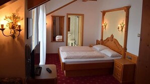 A bedroom with a wooden bed, bedside tables, a mirror, and a TV. - Tannhof (Caldaro Sulla Strada del Vino)