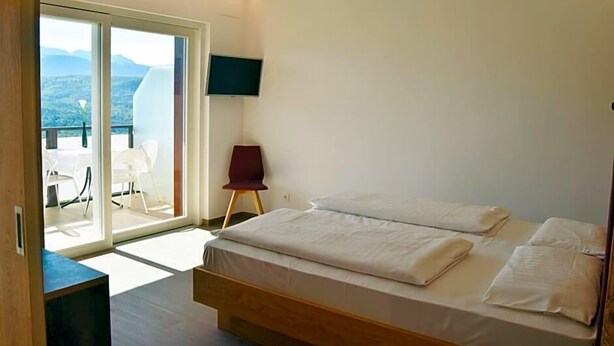 A bedroom with a bed, a TV, a chair, and a balcony with a view. - Tannhof (Caldaro Sulla Strada del Vino)