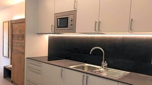 A modern kitchen with a stainless steel sink, white cabinets, and a microwave above the countertop. - Tannhof (Caldaro Sulla Strada del Vino)