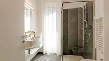 Un baño moderno con ducha envuelta en vidrio, un lavabo blanco y un mueble de tocador con espejo.