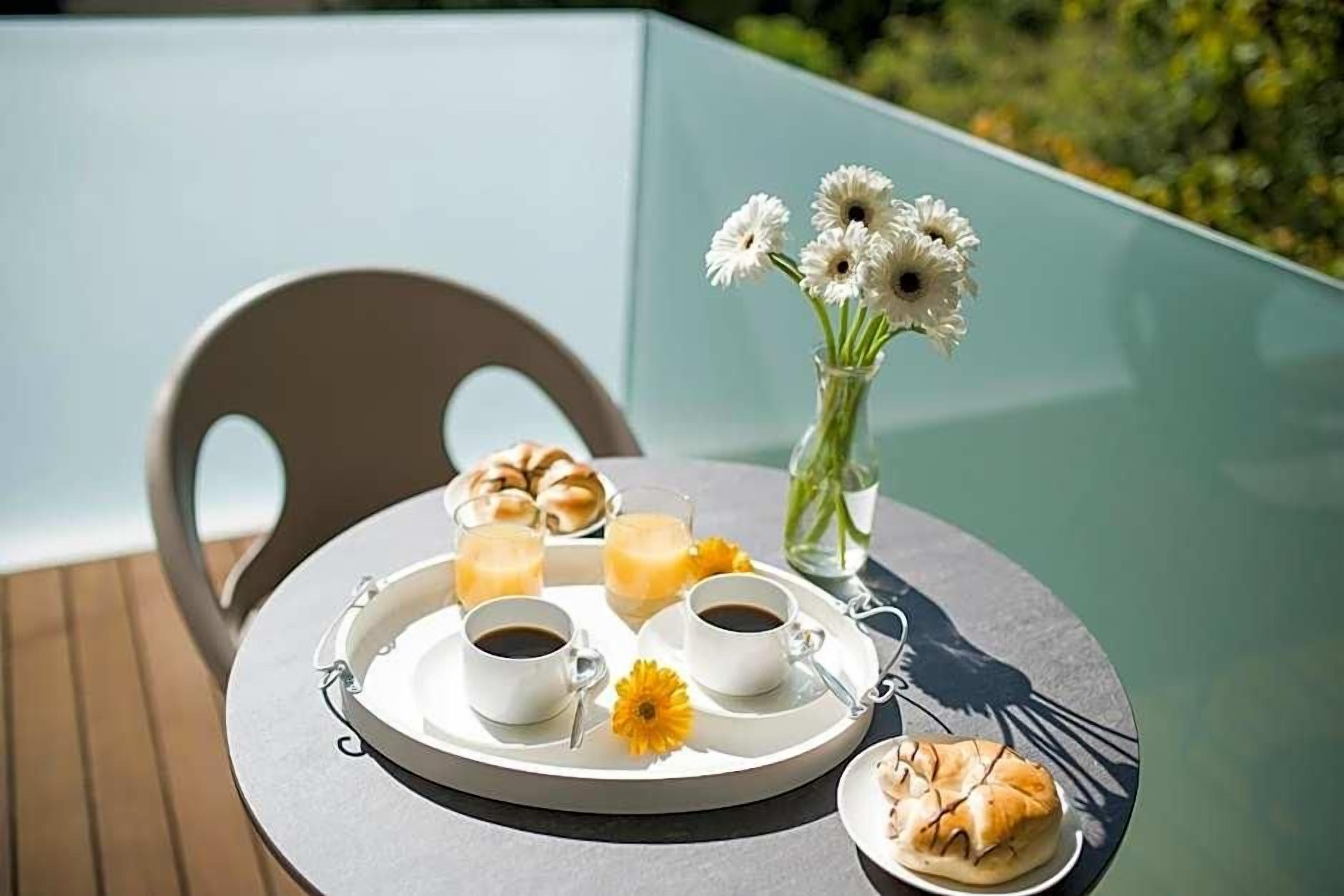 Una mesa con una bandeja de comida y bebidas, una silla y un florero con flores.