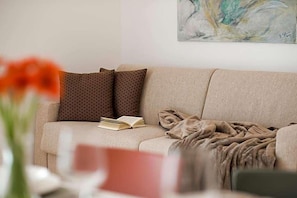 A beige sofa with a book, a blanket, and patterned pillows. - Residence Desiree (Merano)