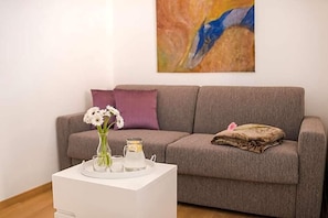 A living room with a grey sofa, a white side table with a vase of flowers, and a painting on the wall. - Residence Desiree (Merano)