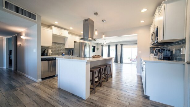 Une cuisine moderne dotée d’un îlot central, d’appareils électroménagers en acier inoxydable et d’un parquet en bois disposé en motif à chevrons.