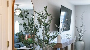 Un couloir avec un grand miroir, un arbre en pot, un banc en bois et un tapis.