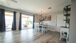 Une pièce spacieuse avec un plancher en bois, une table à manger avec des chaises, un ventilateur de plafond et une porte donnant sur un espace extérieur.