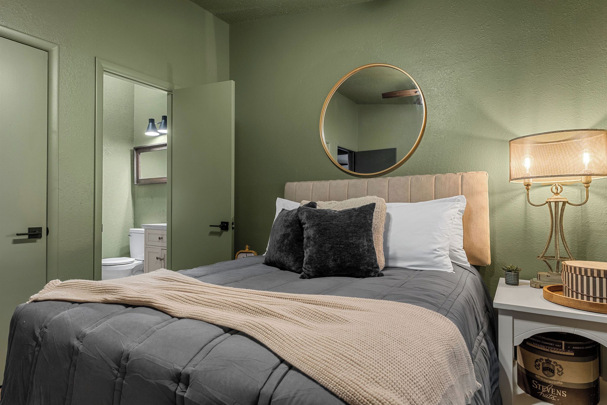 A bedroom with a bed, a bedside lamp, a mirror, and a nightstand.
