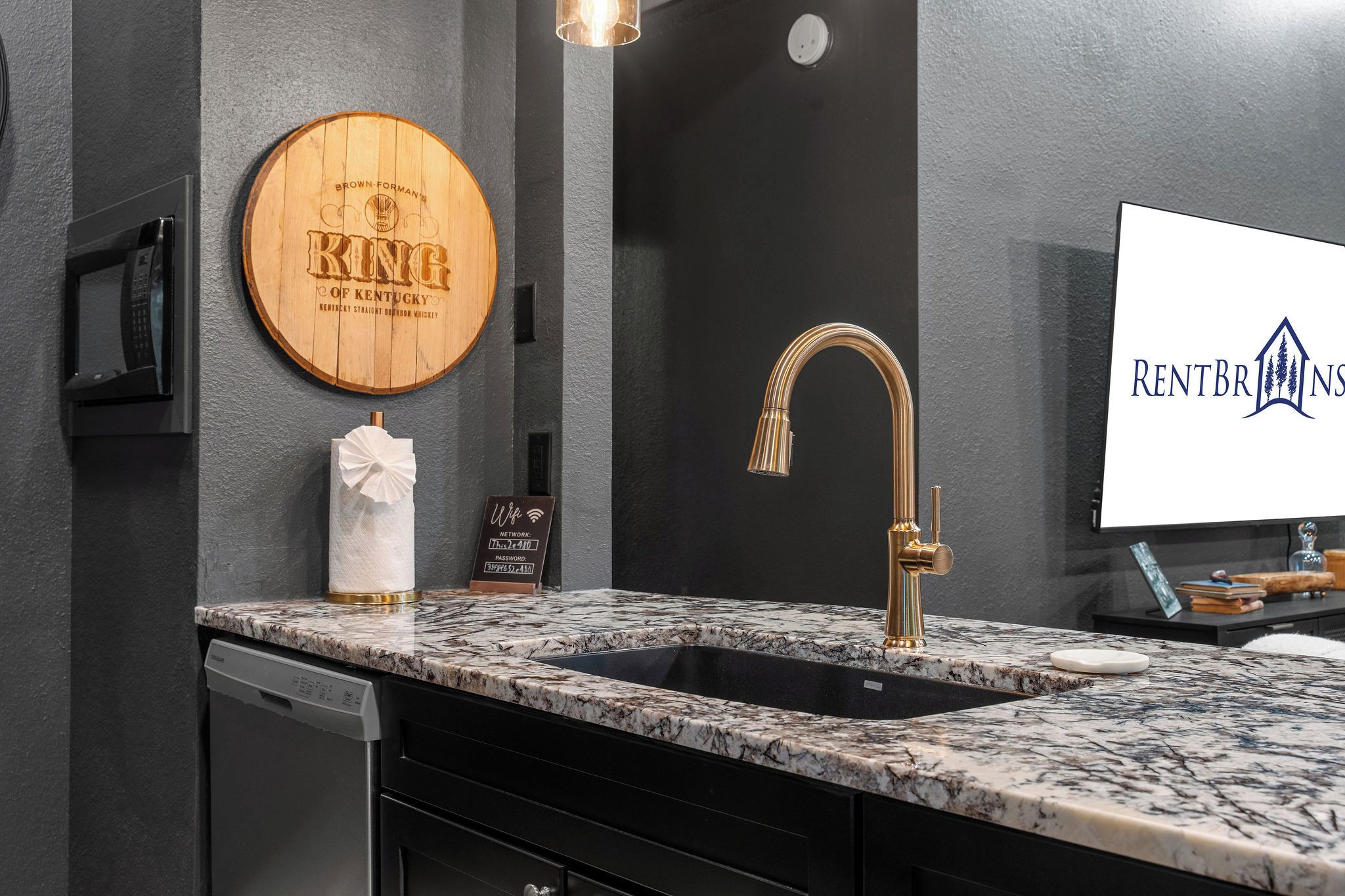 A bathroom with a marble sink, a towel dispenser, and a wooden plaque.