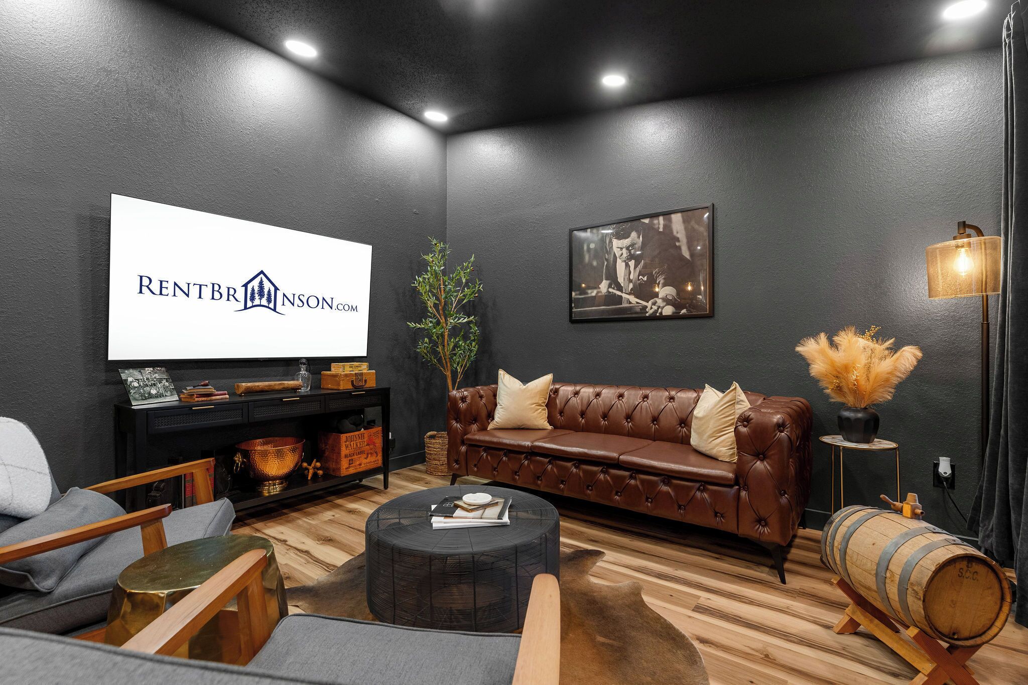 A modern living room with a dark wall, a leather sofa, a coffee table, and a television displaying 'RENTBR INSON.CO'.
