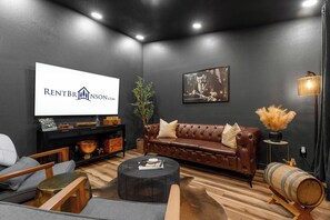 A modern living room with a dark wall, a leather sofa, a coffee table, and a television displaying 'RENTBR INSON.CO'.