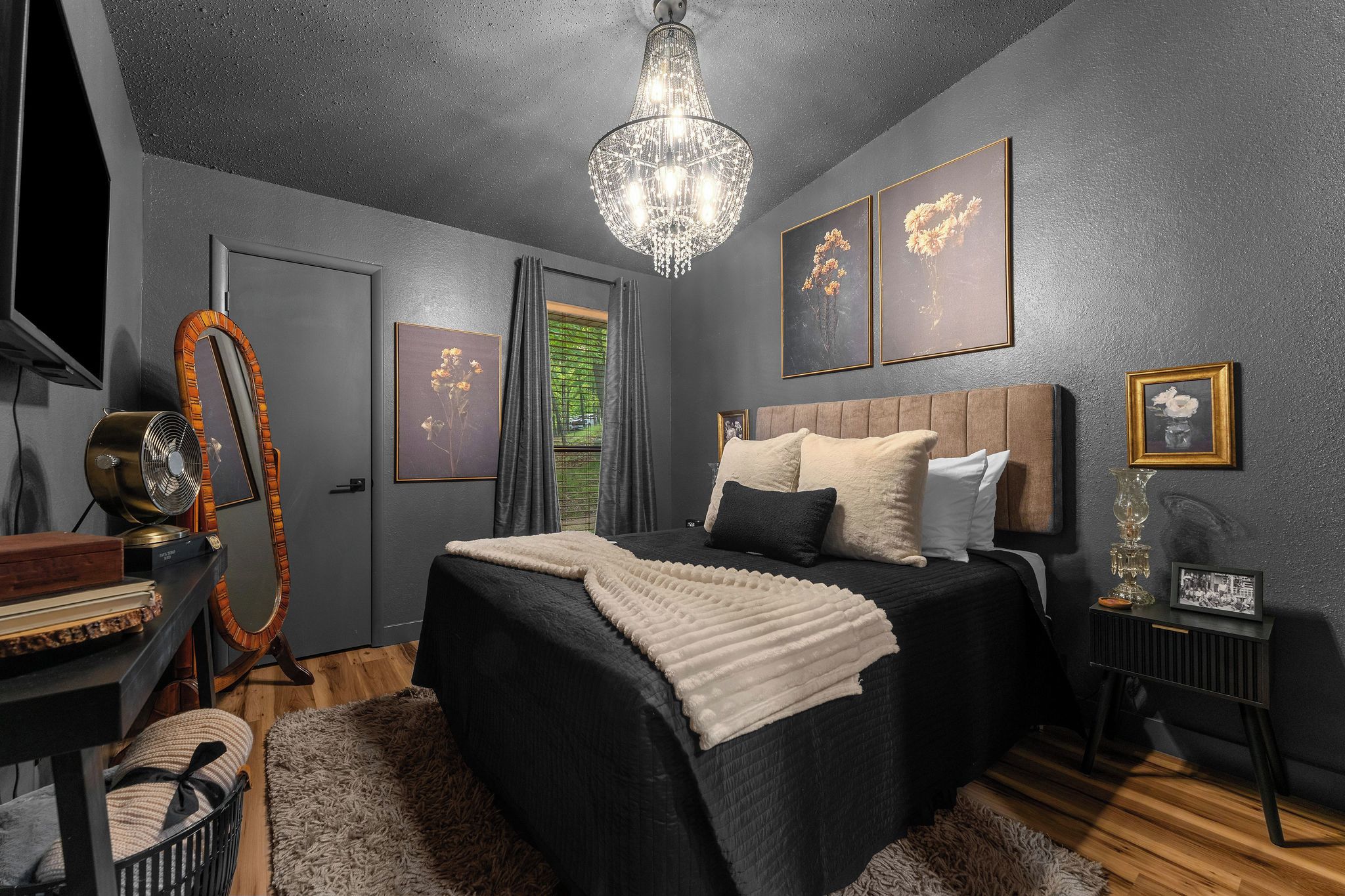 A bedroom with a bed, a dresser, a mirror, a chandelier, and framed artwork on the walls.