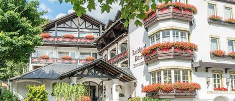 A traditional European hotel with a prominent sign, multiple balconies with flower boxes, and a classic architectural style.