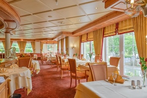 A hotel dining area with multiple tables, chairs, and a view of greenery outside. - Doerr (Bad Laasphe)