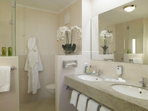 A bathroom with two sinks, a glass shower enclosure, a large mirror, and a vase with white flowers. - Doerr (Bad Laasphe)