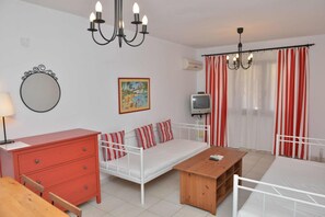 Una habitación con una cama, una mesa de madera, un televisor, un espejo y una araña.