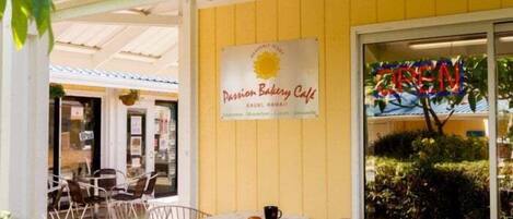 Un café al aire libre con fachada amarilla, un letrero que dice "Passion Bakery Cafe" y mesas en la terraza.
