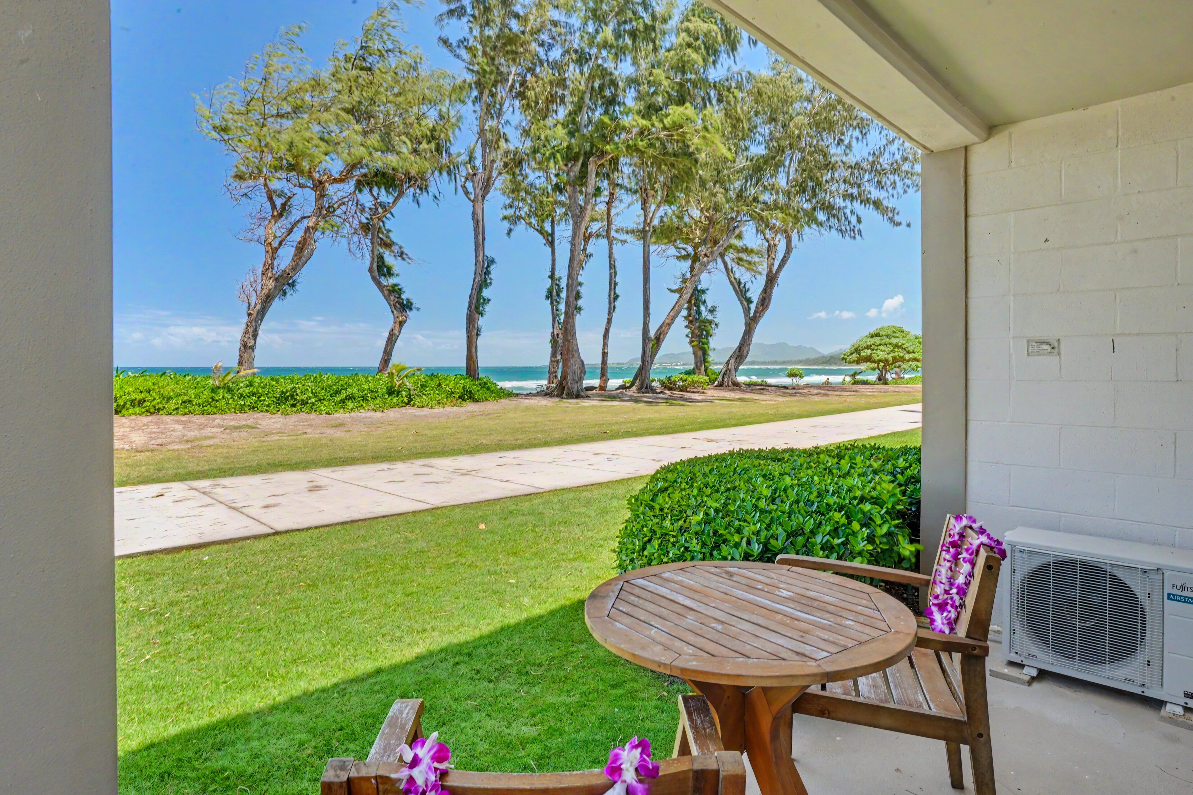 A covered outdoor area with a wooden table and chairs, a view of the ocean, and a white brick wall.