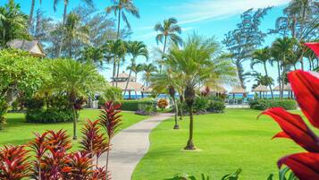 A tropical resort with a well-maintained lawn, palm trees, and a pathway leading to a beach area.