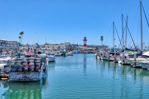A marina with boats docked, a lighthouse in the distance, and a clear blue sky. - Ocean & Marina View Condo with Balcony, Pool, Hot Tub & Gym (Oceanside)