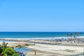 A coastal road with a beach, palm trees, and a clear blue sky. - Ocean & Marina View Condo with Balcony, Pool, Hot Tub & Gym (Oceanside)
