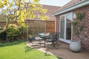 Eine Terrasse mit Tisch und Stühlen, einem Blumentopf und einem Ziegelhaus mit einem Ziegeldach.