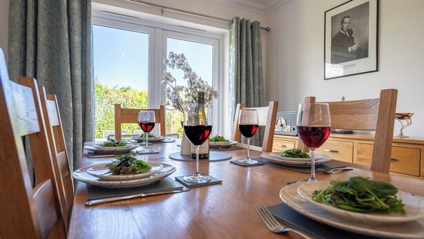 Une table à manger dressée pour quatre personnes, avec des verres à vin, des assiettes de salade et une bouteille de vin.
