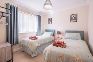 Ein Hotelzimmer mit zwei Betten, einem Schreibtisch, einer Lampe und einem Fenster mit Vorhängen.