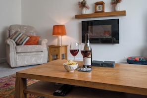 A living room with a wooden coffee table, a sofa, a TV, a fireplace, and a lamp. - Boyd’s Bungalow, Lowestoft (Lowestoft)