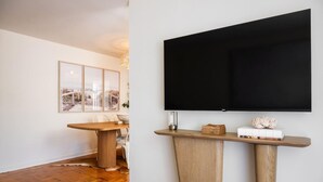 A modern living room with a wooden dining table, a mounted flat-screen TV, and a framed cityscape artwork on the wall. - Light Filled 2BR w/ Balcony & 2 Free Parking (Arlington)