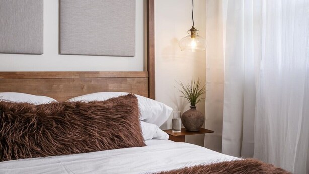 A bedroom with a wooden headboard, a bed with white linens and brown fur throw, a bedside table with a vase and a lamp, and a wall with two framed artworks. - Light Filled 2BR w/ Balcony & 2 Free Parking (Arlington)