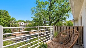 A balcony with a wicker chair, a white railing, and a view of a residential street and trees. - Light Filled 2BR w/ Balcony & 2 Free Parking (Arlington)