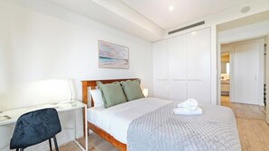 Um quarto com cama, escrivaninha, cadeira e um quadro na parede.