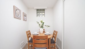 Ein Essbereich mit einem runden Tisch, vier Holzsesseln, weißen Tellern, einer Vase mit Blumen und zwei gerahmten Kunstwerken an der Wand.