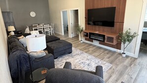 A modern living room with a sofa, ottoman, TV, and ceiling fan.
