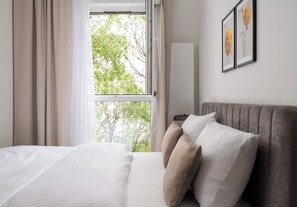 Ein Schlafzimmer mit Bett, einem Fenster mit Vorhängen, einem Nachttisch und einem an der Wand befestigten Kunstwerk.