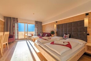 A hotel room with a large bed, a sofa, a dining table, and a balcony with a view. - Berghotel Schopfenhof (Dobbiaco)