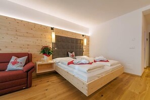 A modern bedroom with a wooden headboard, a single bed, a red armchair, and a bedside table with a plant. - Berghotel Schopfenhof (Dobbiaco)