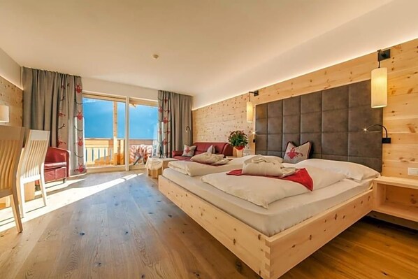 A bedroom with a large bed, a wooden headboard, a balcony, and a view of the sky. - Berghotel Schopfenhof (Dobbiaco)