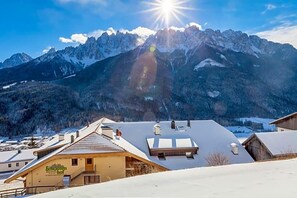 A mountain landscape with a sunlit peak, a snow-covered roof, and a building with a sign. - Berghotel Schopfenhof (Dobbiaco)